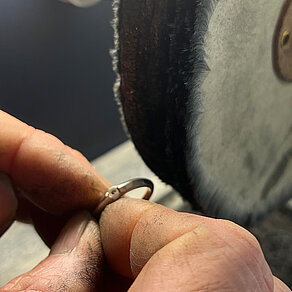 Professionelle Politur in unserer Werkstatt Silberring wird vor einer großen Polierscheibe gehalten